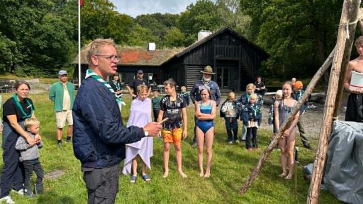 Tropsleder introducere til oprykningsritual for kommende tropsspejdere. mens badeklædte spejdere står i baggrunden