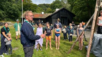 Tropsleder introducere til oprykningsritual for kommende tropsspejdere. mens badeklædte spejdere står i baggrunden